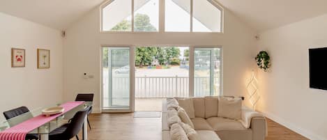 Amplia sala de estar con techo alto, una mesa de comedor con sillas, un sofá y un ventanal con vistas al exterior.