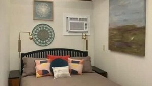 Ein Schlafzimmer mit einem Bett, einer Wand-Klimaanlage, einer Uhr und einem Gemälde.