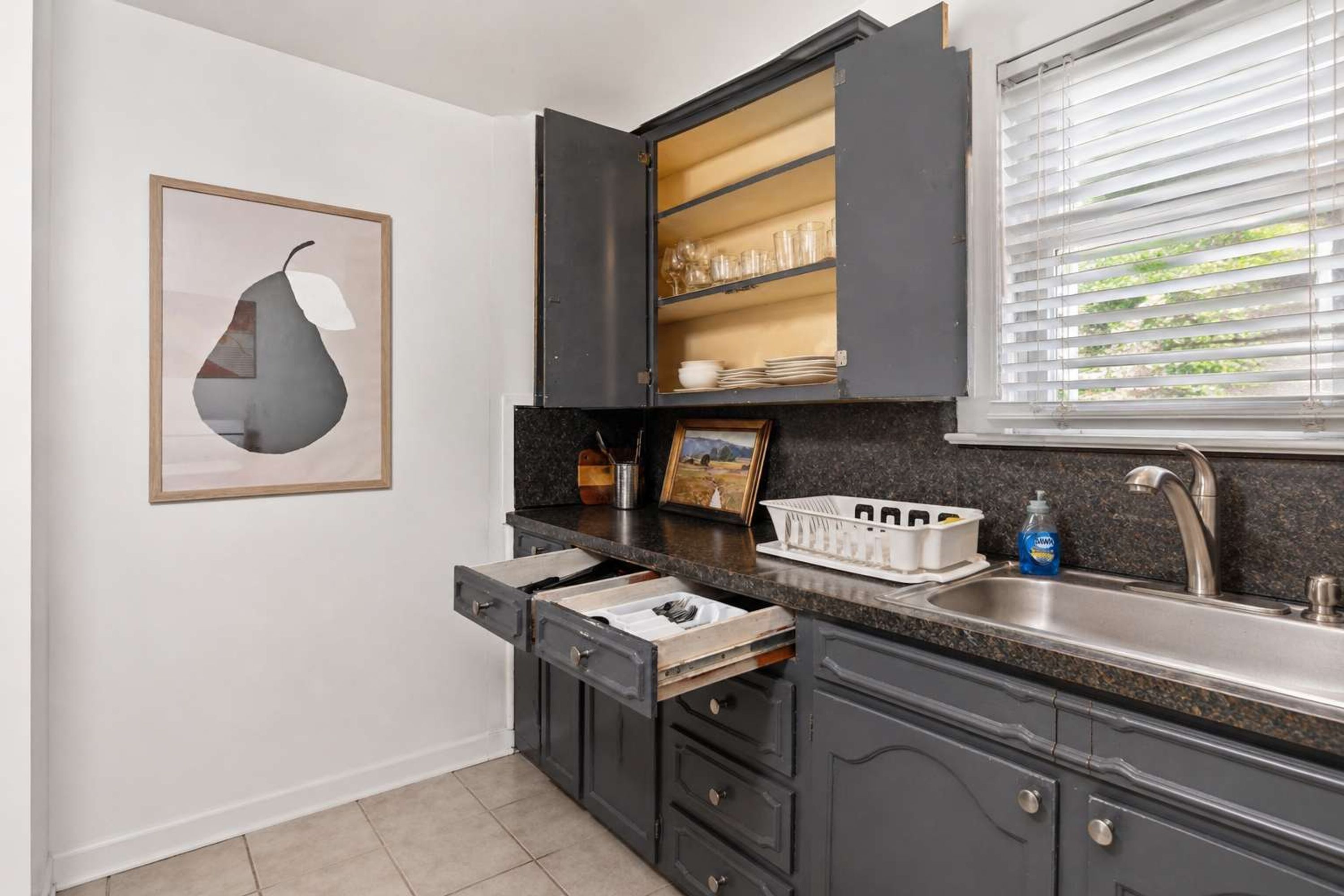 A kitchen with dark cabinets, a countertop, a sink, and a window with blinds.