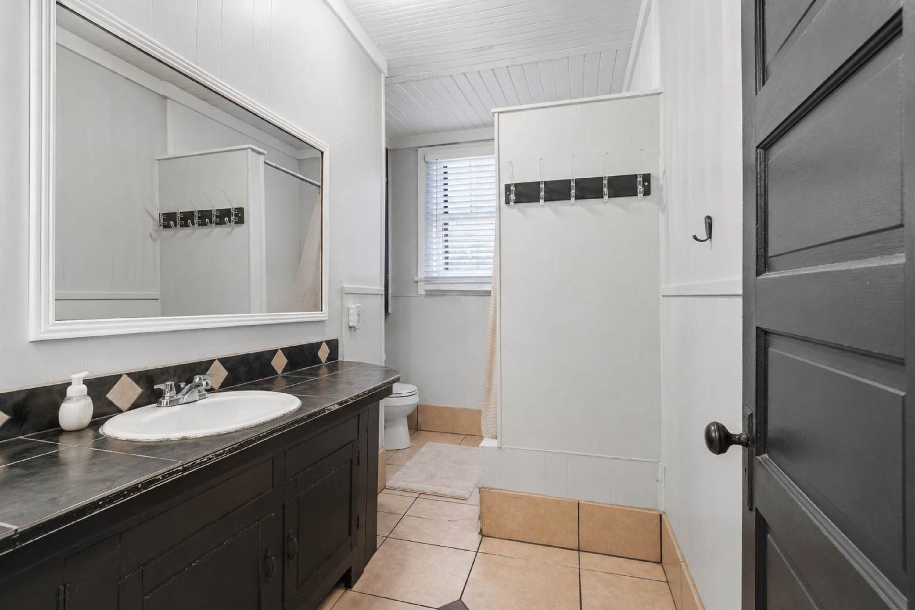 Un baño con lavamanos blanco, muebles oscuros, un espejo grande y una puerta con pomo.