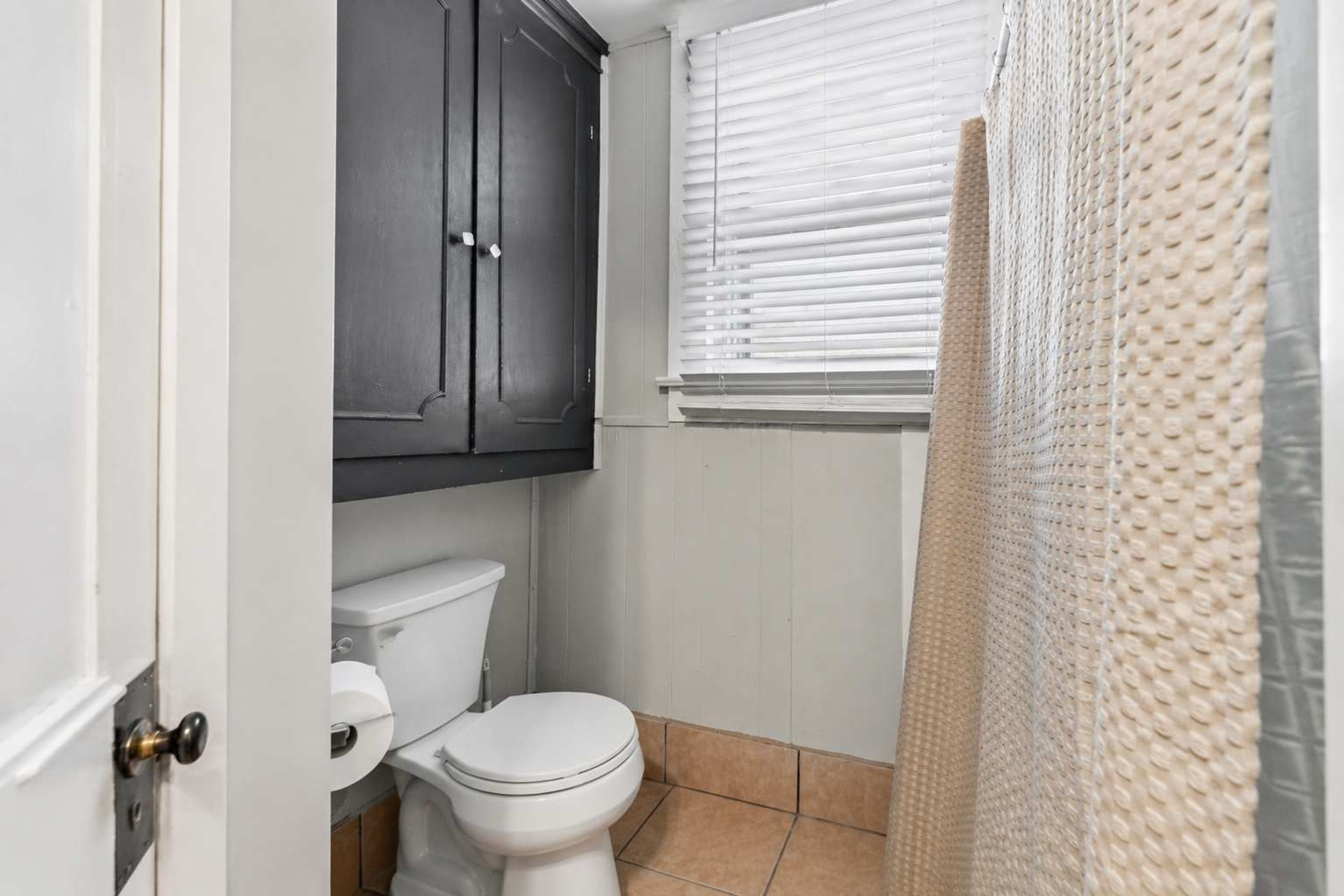 A bathroom with a toilet, a dark cabinet, and a window with blinds.
