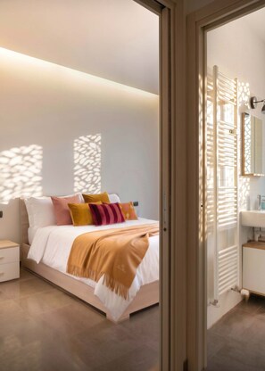 Ein modernes Schlafzimmer mit Bett, Nachttisch und einem durchgehenden Türrahmen sichtbarem Badezimmer.