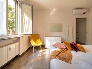 Ein Schlafzimmer mit einem Bett, einem Sessel, einem Schminktisch, einem Spiegel und einem Fenster mit Vorhängen.