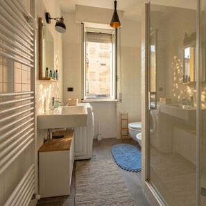 Ein modernes Badezimmer mit einer Duschkabine aus Glas, einem weißen Waschbecken und einem Fenster für natürliches Licht.
