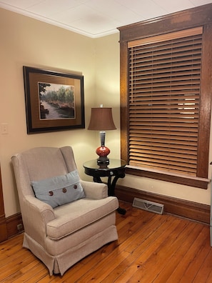 A room with a herringbone-patterned armchair, a framed painting, a table lamp, and a window with wooden blinds. - 3-bedroom condo in adorable Elk Rapids with AC and comfort - One block to beach (Elk Rapids)