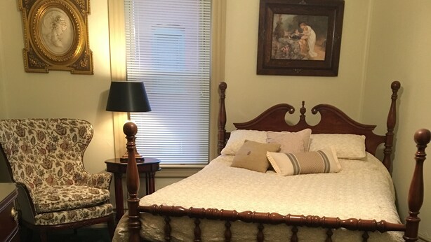 A bedroom with a four-poster bed, a chair, a lamp, and two framed pictures on the walls. - 3-bedroom condo in adorable Elk Rapids with AC and comfort - One block to beach (Elk Rapids)