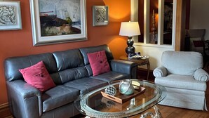 A living room with a leather sofa, a glass coffee table, and a light-colored armchair. - 3-bedroom condo in adorable Elk Rapids with AC and comfort - One block to beach (Elk Rapids)