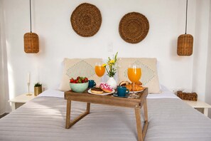 Ein ordentlich bezogenes Bett mit Frühstückstablett, zwei gewebten Wandbehängen und zwei hängenden Korbmöbellampen.