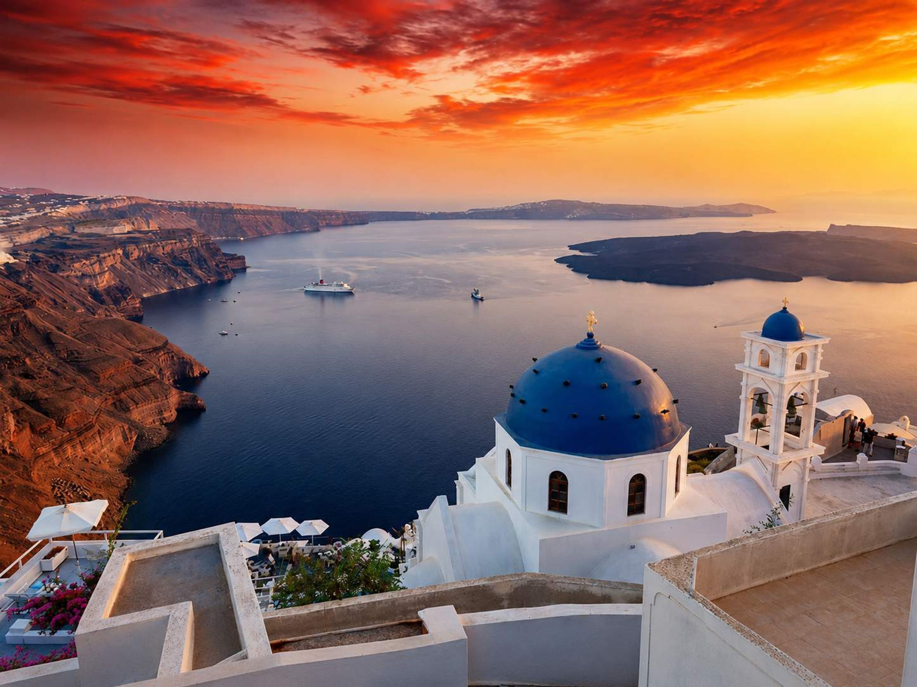 A coastal view with a white building featuring a blue dome and bell tower, overlooking a calm sea and cliffs.