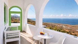 Ein Balkon mit weißem Tisch, einer grünen Tür und Blick auf das Meer und die Landschaft.