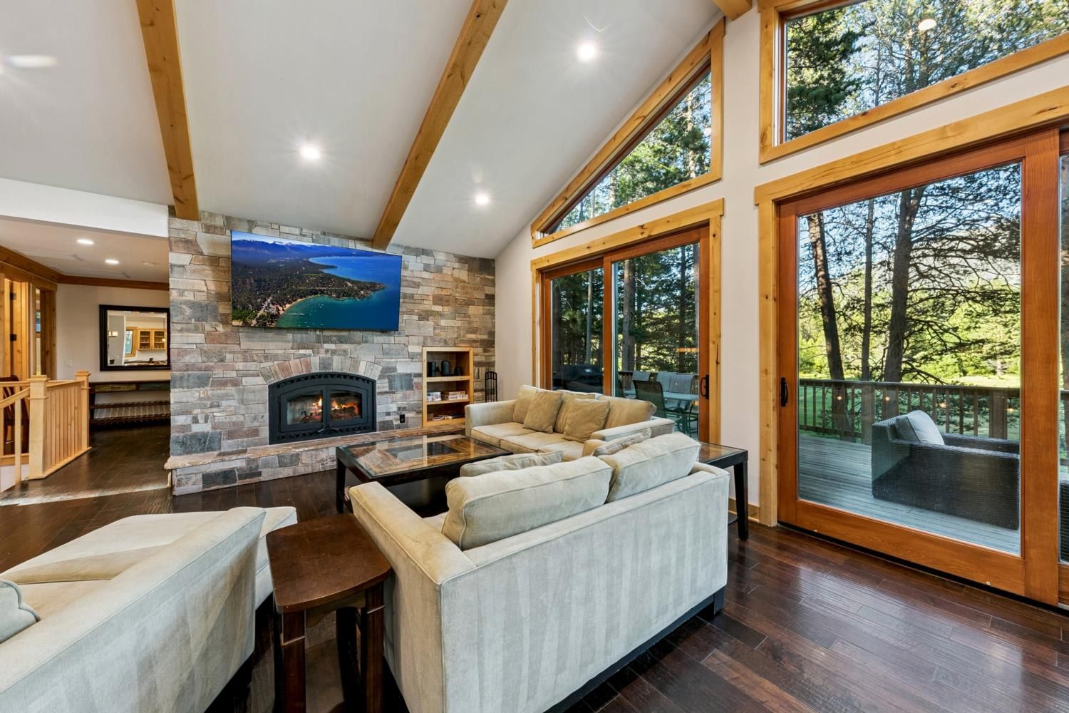 A spacious living room with a stone fireplace, a large sofa, and a view of the outdoors through large windows.