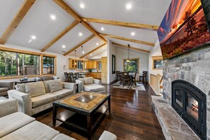 A spacious living area with a fireplace, wooden beams, and a dining area. - The Alpine Green Lodge (South Lake Tahoe)