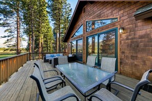 A wooden deck with outdoor furniture, a glass table, and a view of a forested area. - The Alpine Green Lodge (South Lake Tahoe)