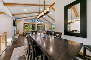 A spacious dining area with a long table, multiple chairs, and a modern chandelier. - The Alpine Green Lodge (South Lake Tahoe)