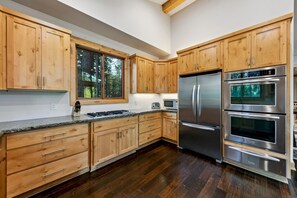 Een moderne keuken met houten kastjes, roestvrijstalen apparatuur en een groot raam.