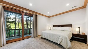 Quarto com uma cama grande, duas luminárias de cabeceira, mesa de cabeceira e vista para uma varanda com guarda-corpo de madeira.