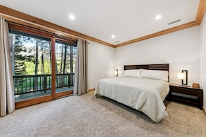 A bedroom with a large bed, two bedside lamps, a nightstand, and a view of a balcony with a wooden railing. - The Alpine Green Lodge (South Lake Tahoe)
