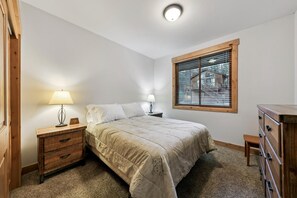 A bedroom with a bed, nightstands, a dresser, a window with blinds, and a ceiling light. - The Alpine Green Lodge (South Lake Tahoe)