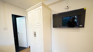 A room with a white wardrobe, a television mounted on the wall, and a white trash bin. - RQ Opsian Ratchada Service Apartments (Bangkok)