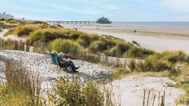 A sandy beach with dunes, a pier, and a building in the distance. - Cosy apartment for 6 people with WIFI and TV (Blankenberge)