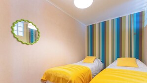 A room with two beds, each with a yellow blanket, a striped wall, and a green-framed mirror. - Cosy apartment for 6 people with WIFI and TV (Blankenberge)