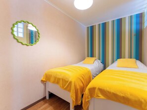Ein Zimmer mit zwei Betten, jeweils mit einer gelben Decke, einer gestreiften Wand und einem spiegelnden Rahmen in Grün.