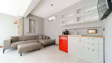A modern kitchen with white cabinets and a red appliance, a beige sectional sofa, and a stone accent wall.