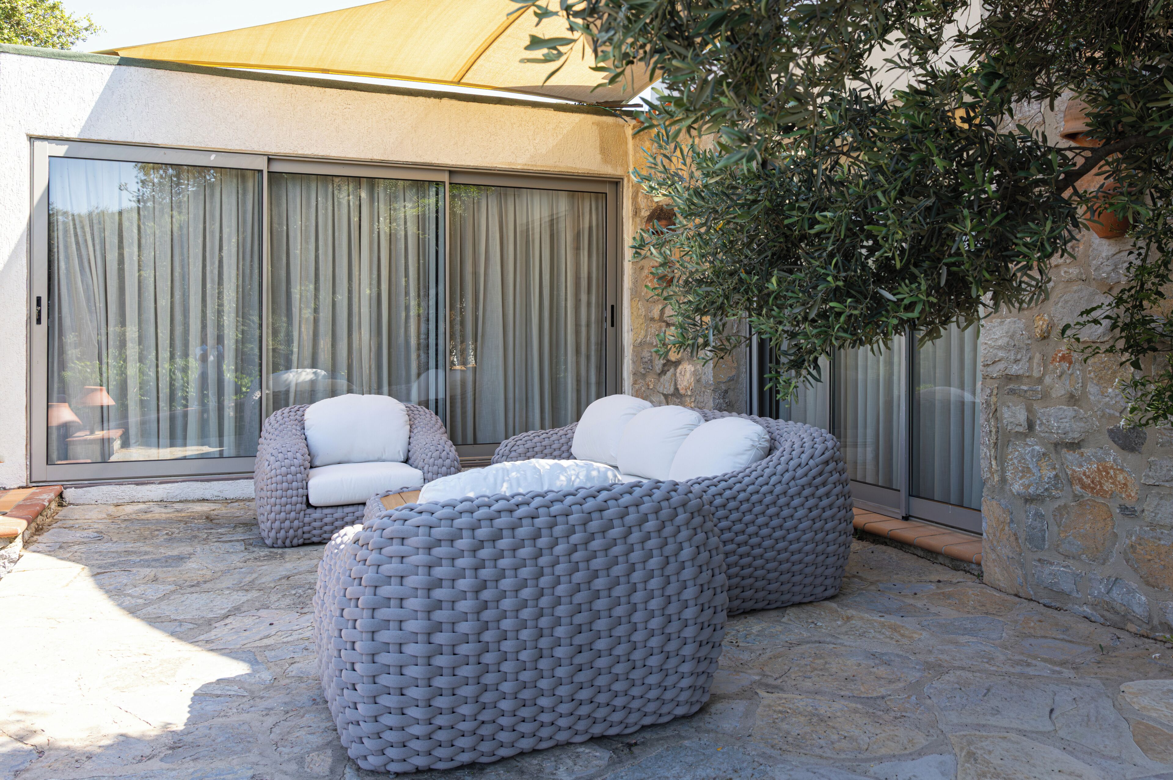 Une terrasse dotée de deux canapés gris en fibres tressées, d’un sol en pierre et d’une grande porte-fenêtre coulissante.