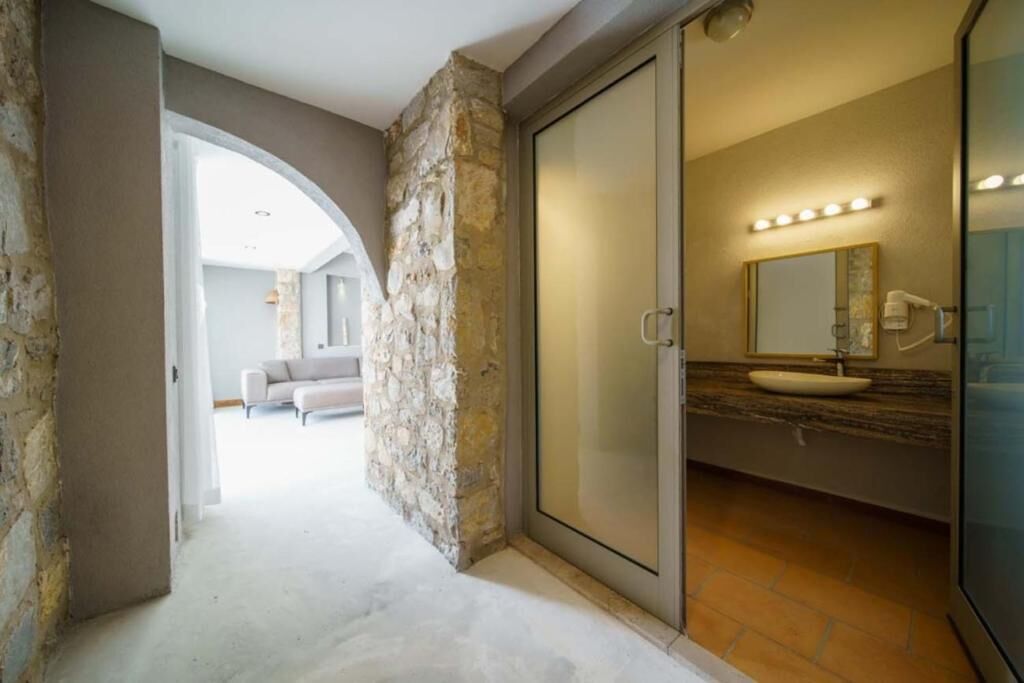 A bathroom with a stone wall, a sliding door, a sink, a mirror, and a lighted vanity.