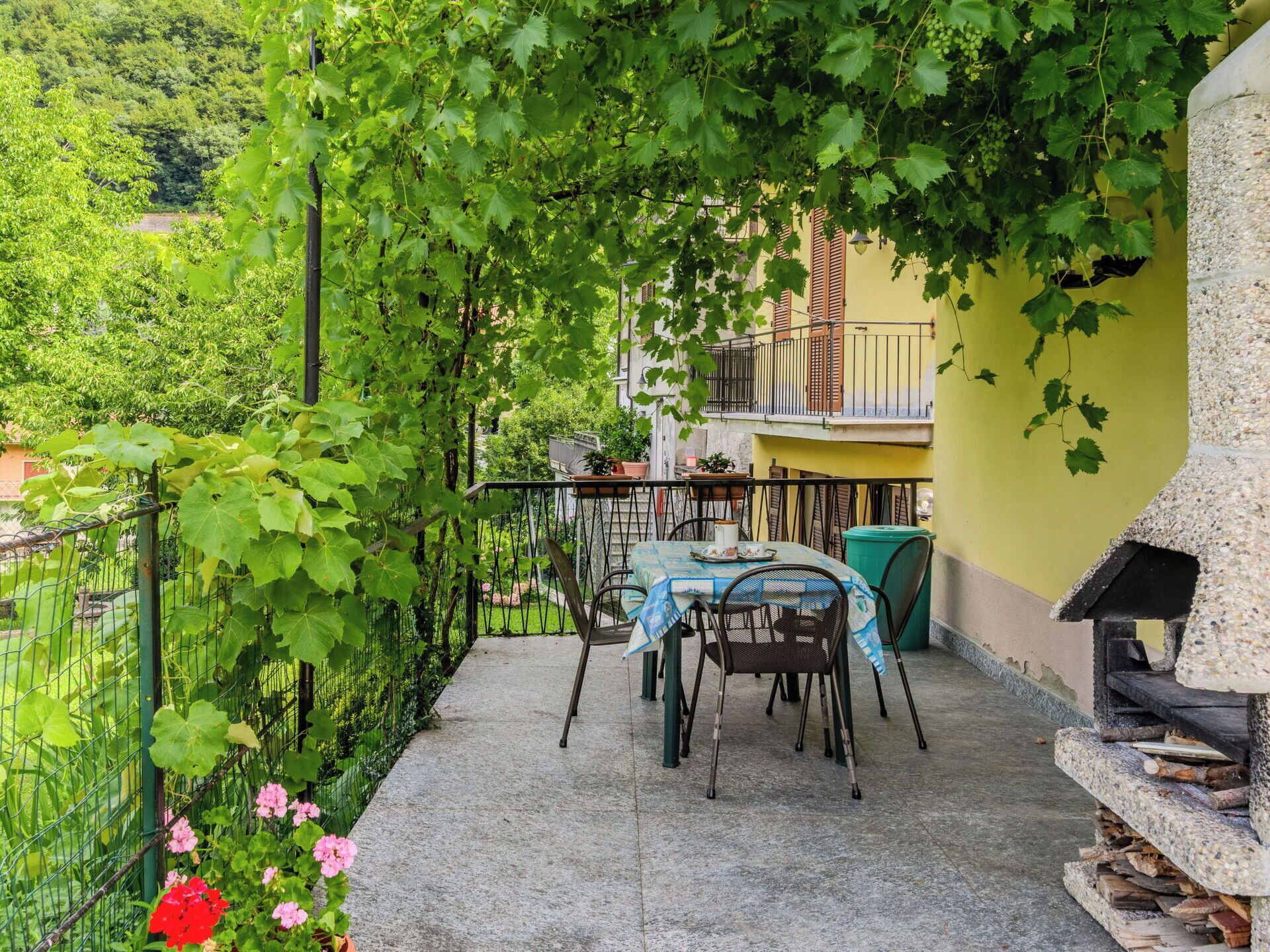 Eine Terrasse mit Tisch und Stühlen, umgeben von viel Grün und einer Steinstruktur.