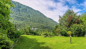 Een weelderige tuin met een houten pergola, verschillende planten en een berg op de achtergrond.