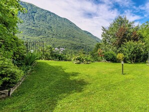 Ein üppiger Garten mit einer Holz-Pergola, vielfältigen Pflanzen und einem Berg im Hintergrund.