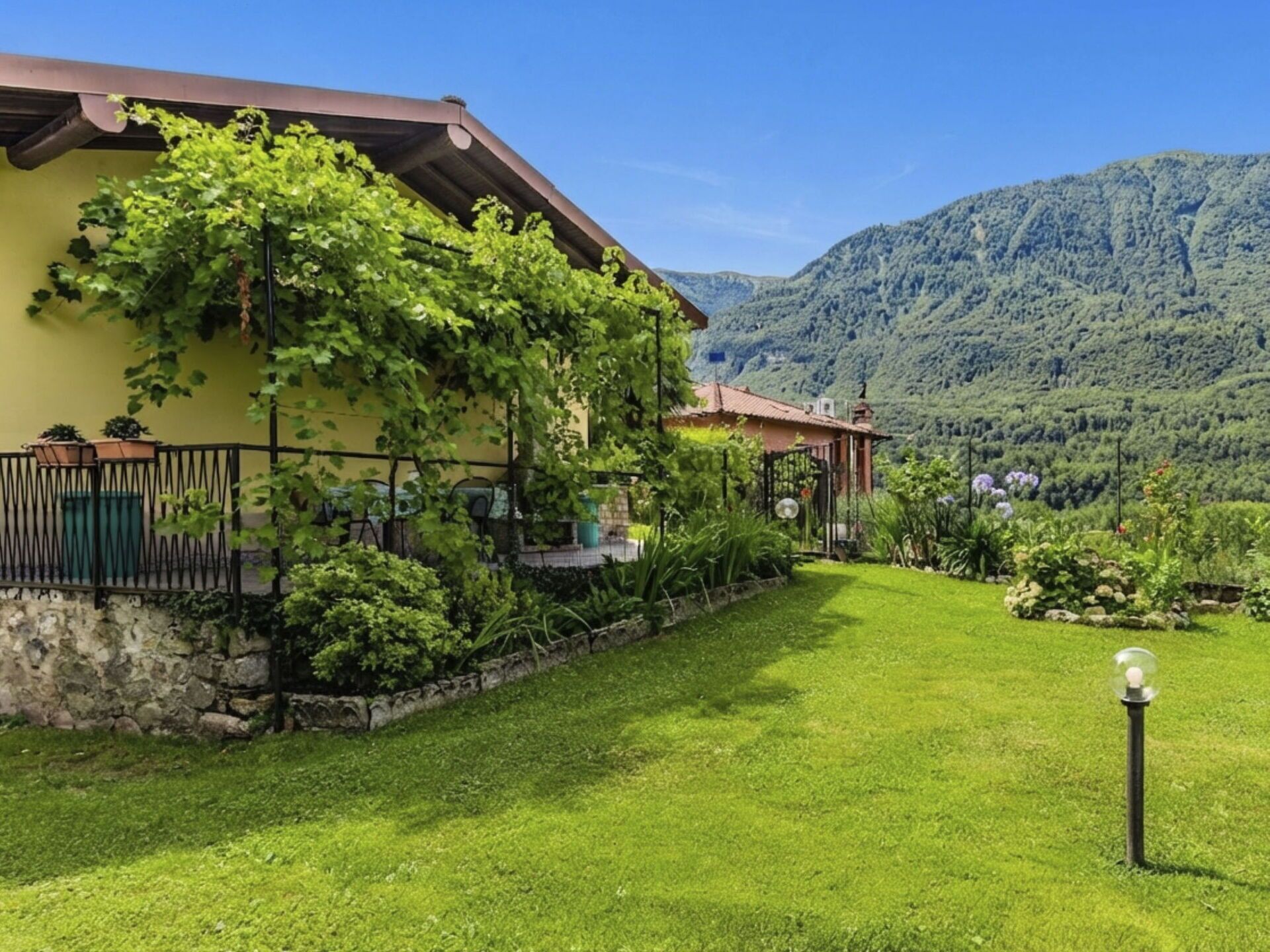 Uma casa com um jardim, uma montanha ao fundo e um céu limpo.