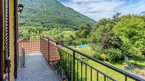 Een balkon met uitzicht op een bergachtig landschap, een zwembad en een omheind tuingedeelte.