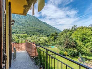 Ein Balkon mit Blick auf eine gebirgige Landschaft, ein Pool und ein eingezäunter Gartenbereich.