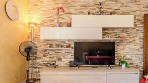 Un salon moderne doté d’un téléviseur à écran plat, d’un ventilateur sur pied et d’un mur décoratif orné d’un motif en pierre.