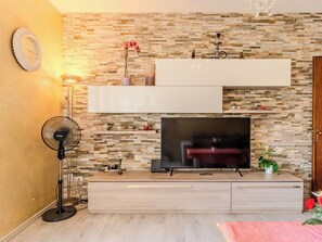 Ein modernes Wohnzimmer mit Flachbildfernseher, Standventilator und dekorativer Wand mit Steinmuster.