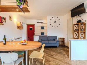 Ein modernes Wohnzimmer mit Essbereich, einem grauen Sofa, einem Holzesstisch und einer Wanduhr.