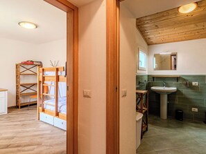 Ein Zimmer mit einem Holzbett, einem Regal mit Kisten, einem Badezimmer mit Waschbecken und Spiegel sowie einem gefliesten Boden.