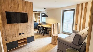 Ein moderner Wohnraum mit Holzwand, Flachbildfernseher, Essbereich und Sofa.