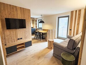 Ein moderner Wohnraum mit Holzwand, Flachbildfernseher, Essbereich und Sofa.