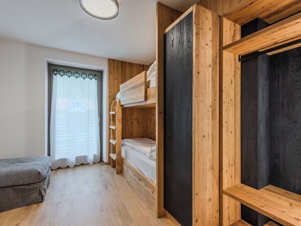 Ein Zimmer mit einem Bett, einer Bank, einem Fenster mit Vorhängen und Holzregalen.