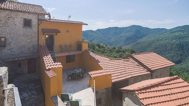 A stone building with a yellow exterior and a red-tiled roof, featuring a small outdoor seating area with chairs and a table. - Beautiful private villa for 4 people with WIFI and terrace (Bagnone)