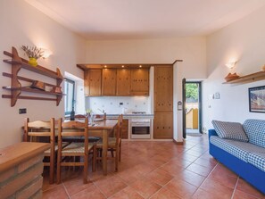 Een compacte keuken met houten kastjes, een eettafel met stoelen en een blauwe bank in een lichte kamer met betegelde vloer.