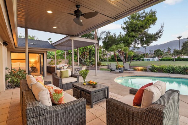 Une terrasse extérieure aménagée avec des meubles en osier, une piscine et un espace couvert doté d’un ventilateur de plafond.