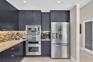 A modern kitchen with dark cabinets, stainless steel appliances, and a tiled backsplash. - Elegant South-end (Less Wind) 3BD/3BA Right On The Fairway! (Palm Springs)