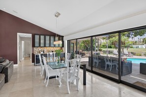 Une cuisine moderne avec un coin repas vitré et une grande porte-fenêtre coulissante donnant sur la piscine.
