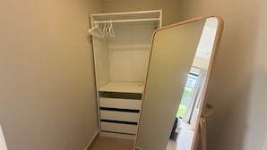 Un vestidor pequeño con espejo, barra para colgar ropa y algunos cajones.