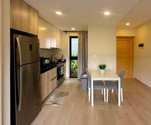 A modern kitchen with a refrigerator, stove, and microwave. There is a dining area with a table and chairs, and a potted plant on the table. - NOK Stylish 1BR in Ventura By Vistacana Rentals (Punta Cana)