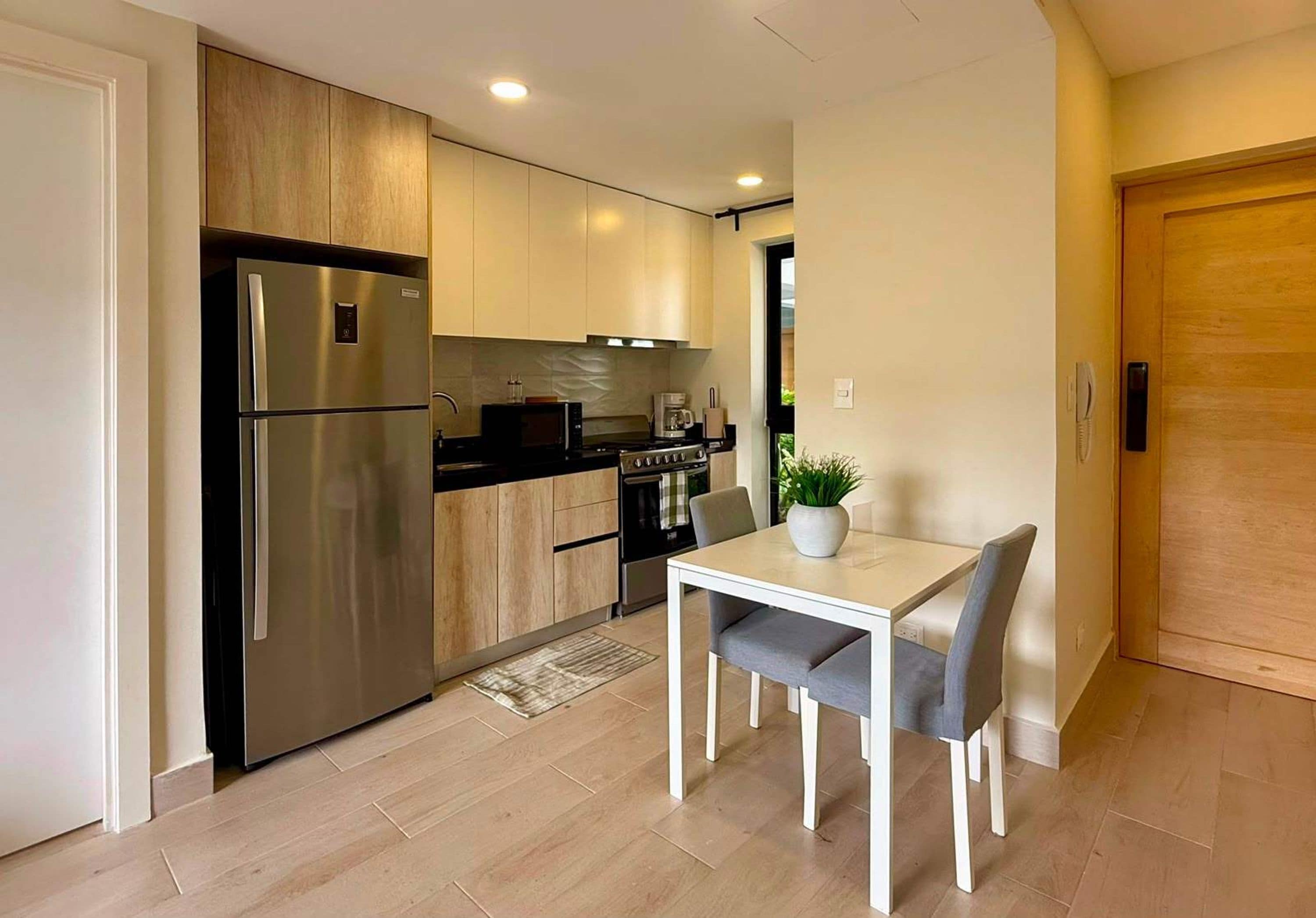 Una cocina moderna con un refrigerador de acero inoxidable, armarios de madera, una mesa de comedor con sillas y una planta en maceta.